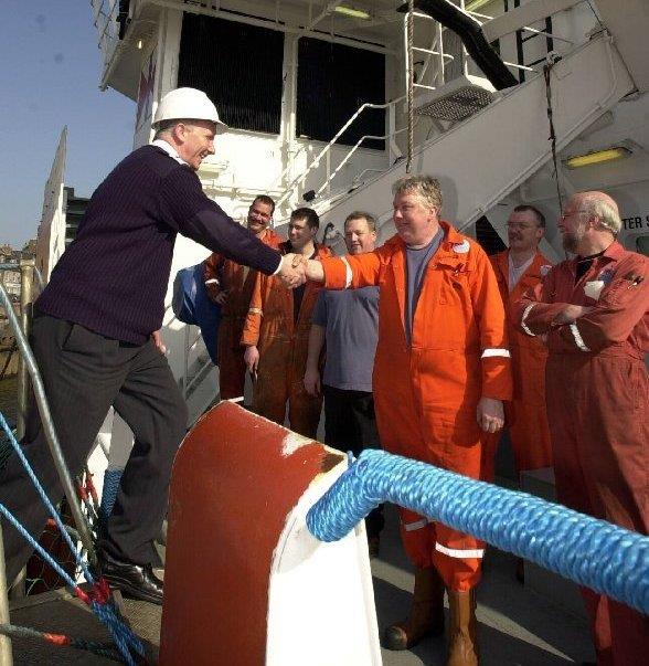 Group of seafarers welcoming a ship visitor on board. One of the seafarers is shaking hands with the visitor.