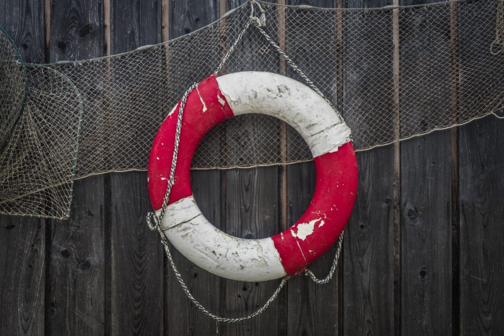 Image of a red and white life saver and fishing net hanging on a wooden fence.
